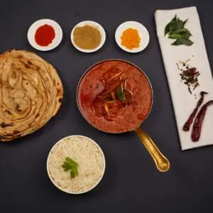 Traditional tikka masala with naan bread, rice, and spices on a dark background.