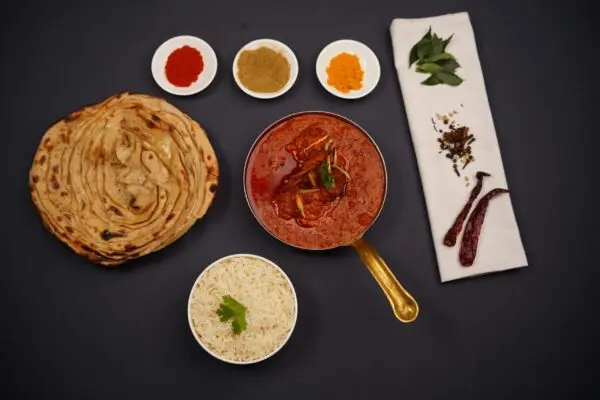 Traditional tikka masala with naan bread, rice, and spices on a dark background.