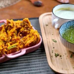 Delicious Indian pakora served with green chutney on a wooden tray.