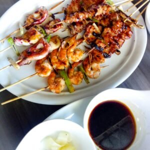 Delicious grilled skewers including shrimp and squid served with sauce on a white plate.