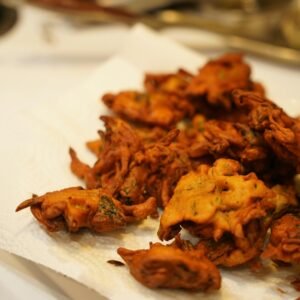 Golden brown Indian pakoras freshly fried and resting on paper towel in kitchen setting.