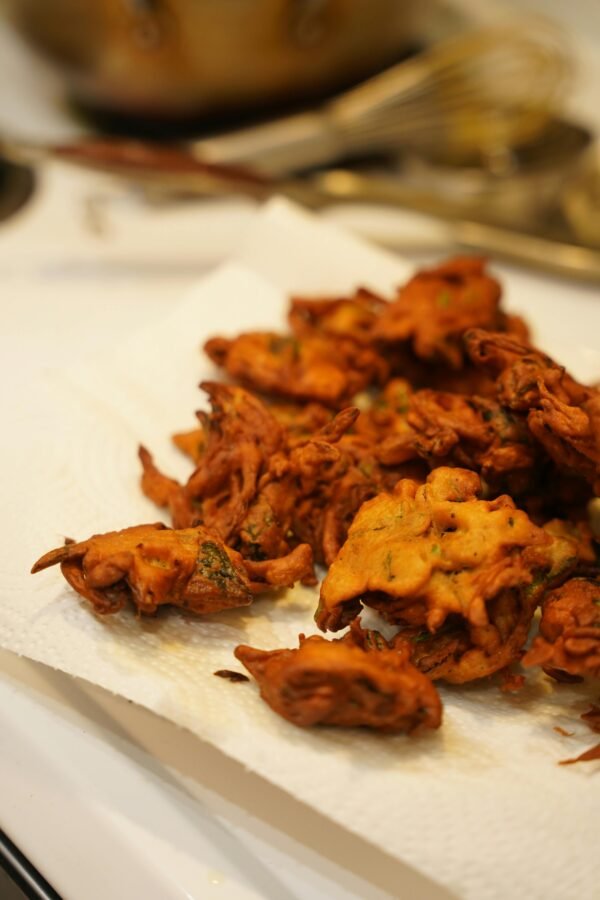 Golden brown Indian pakoras freshly fried and resting on paper towel in kitchen setting.